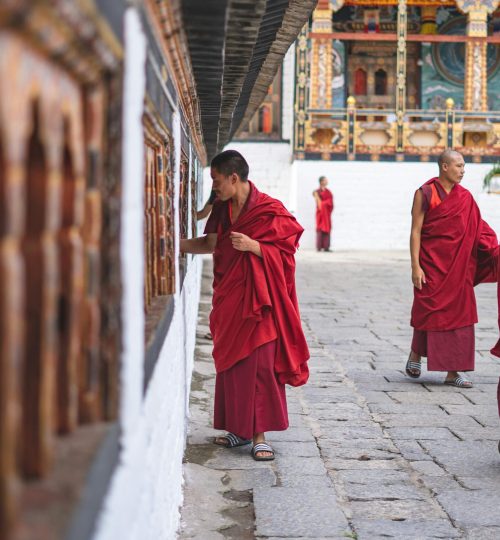 Buddhist monks in red robes walking and interacting in a Bhutan temple courtyard.