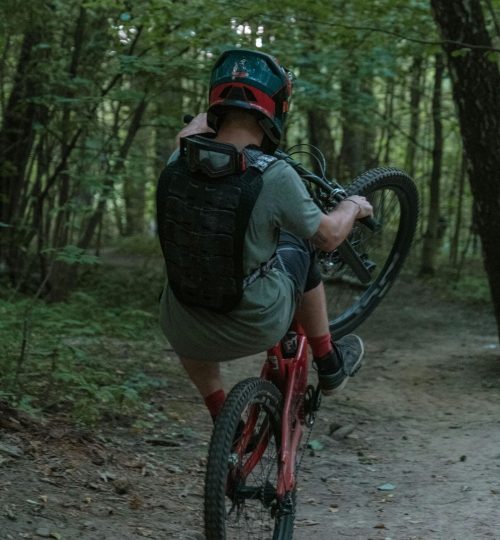 A mountain biker performs a wheelie on a forest trail, showcasing skill and adventure.